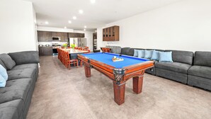 A modern living room with a pool table, grey sofas, and a dining area with orange chairs. - Private Retreat:master suite w Jacuzzi tub,game room,pool,outdoor entertainment! (North Myrtle Beach)