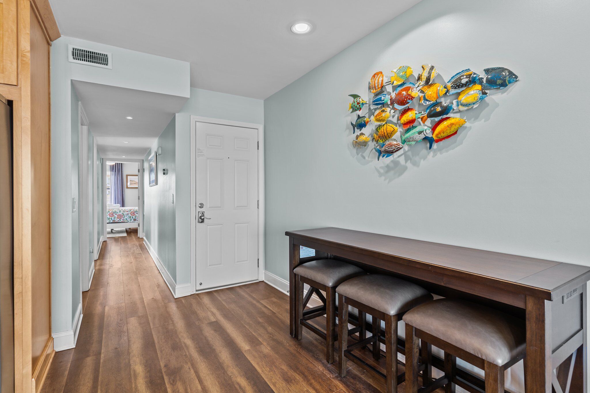 A hallway with wooden flooring, a white door, and a wall with colorful fish artwork.