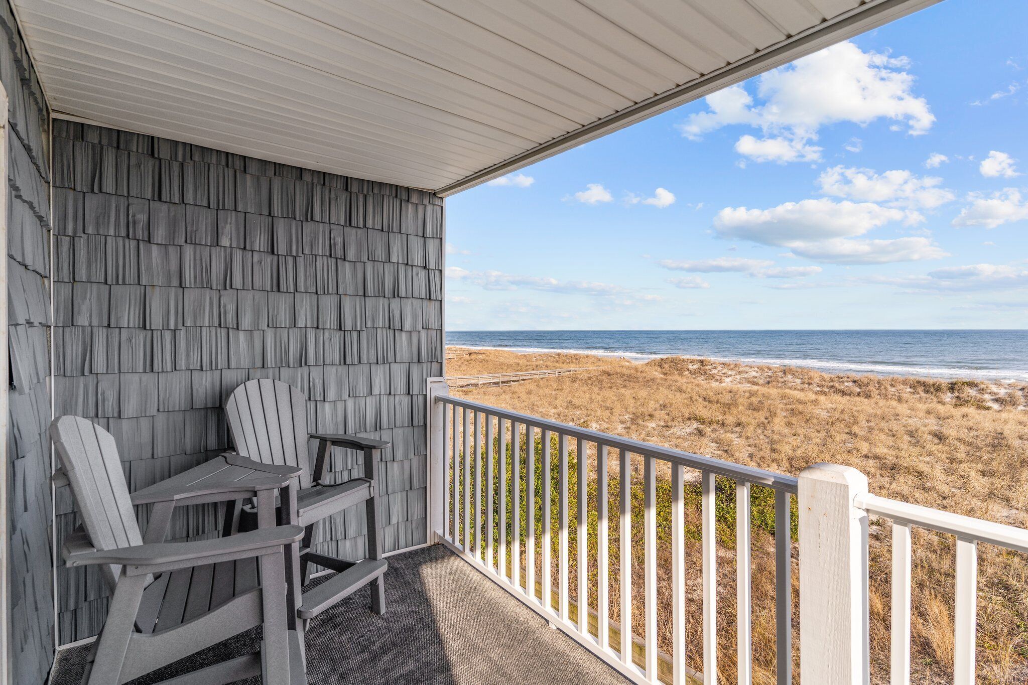 Un espacio de estar al aire libre techado con sillas Adirondack y vistas a la playa.