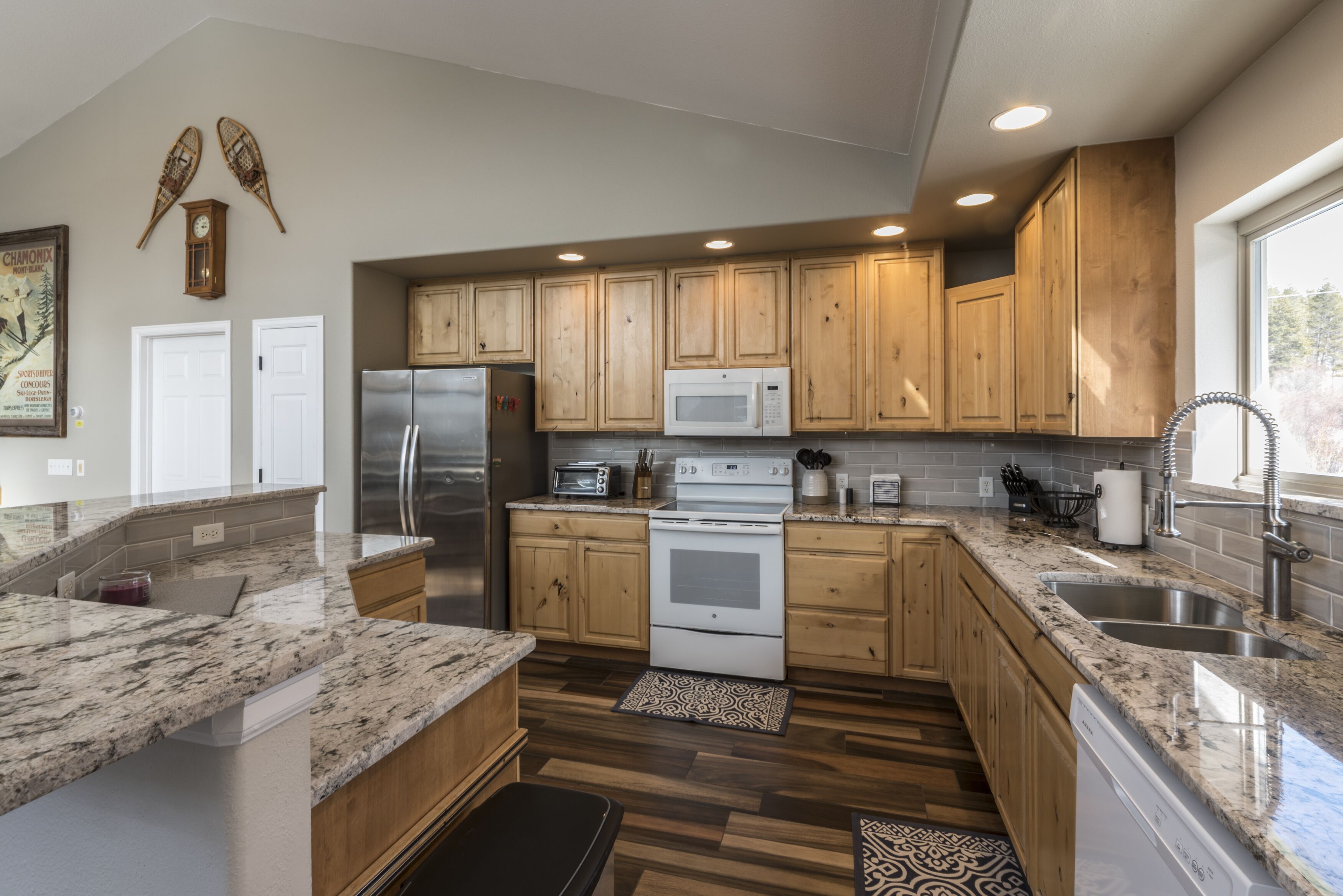 A modern kitchen with wooden cabinets, granite countertops, stainless steel appliances, and a large window providing natural light.