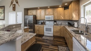 A modern kitchen with wooden cabinets, granite countertops, stainless steel appliances, and a large window providing natural light. - Breathtaking Mountain Sunsets! 6BR, 3 King Beds, Hot Tub, Shuttle, Sleeps 16+ (Fraser)