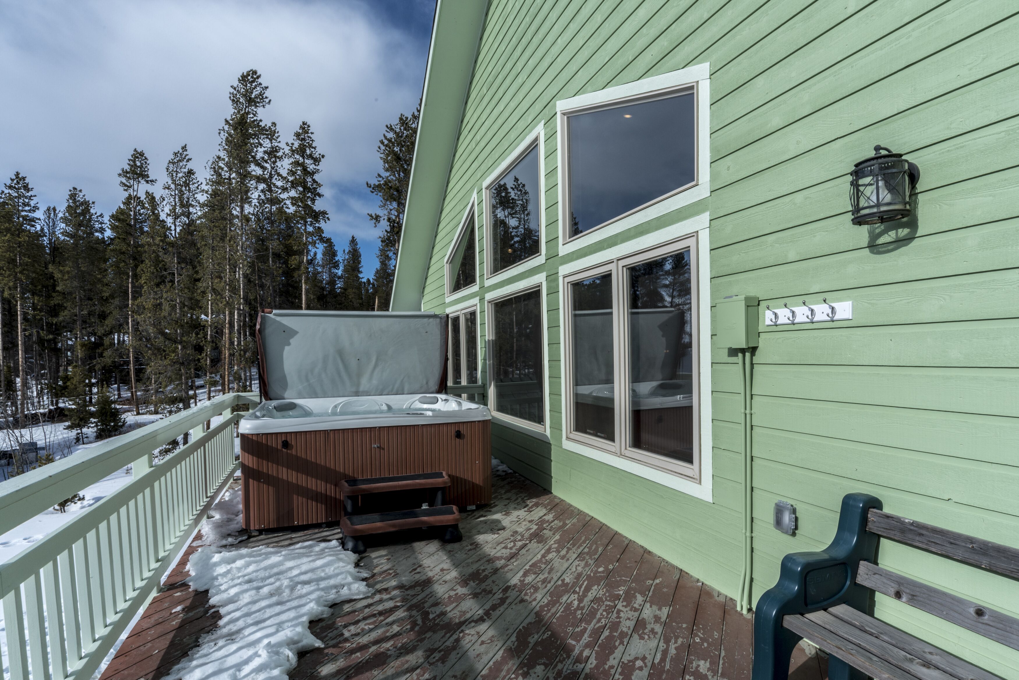 Une terrasse en bois avec un jacuzzi, un banc et un espace abrité.