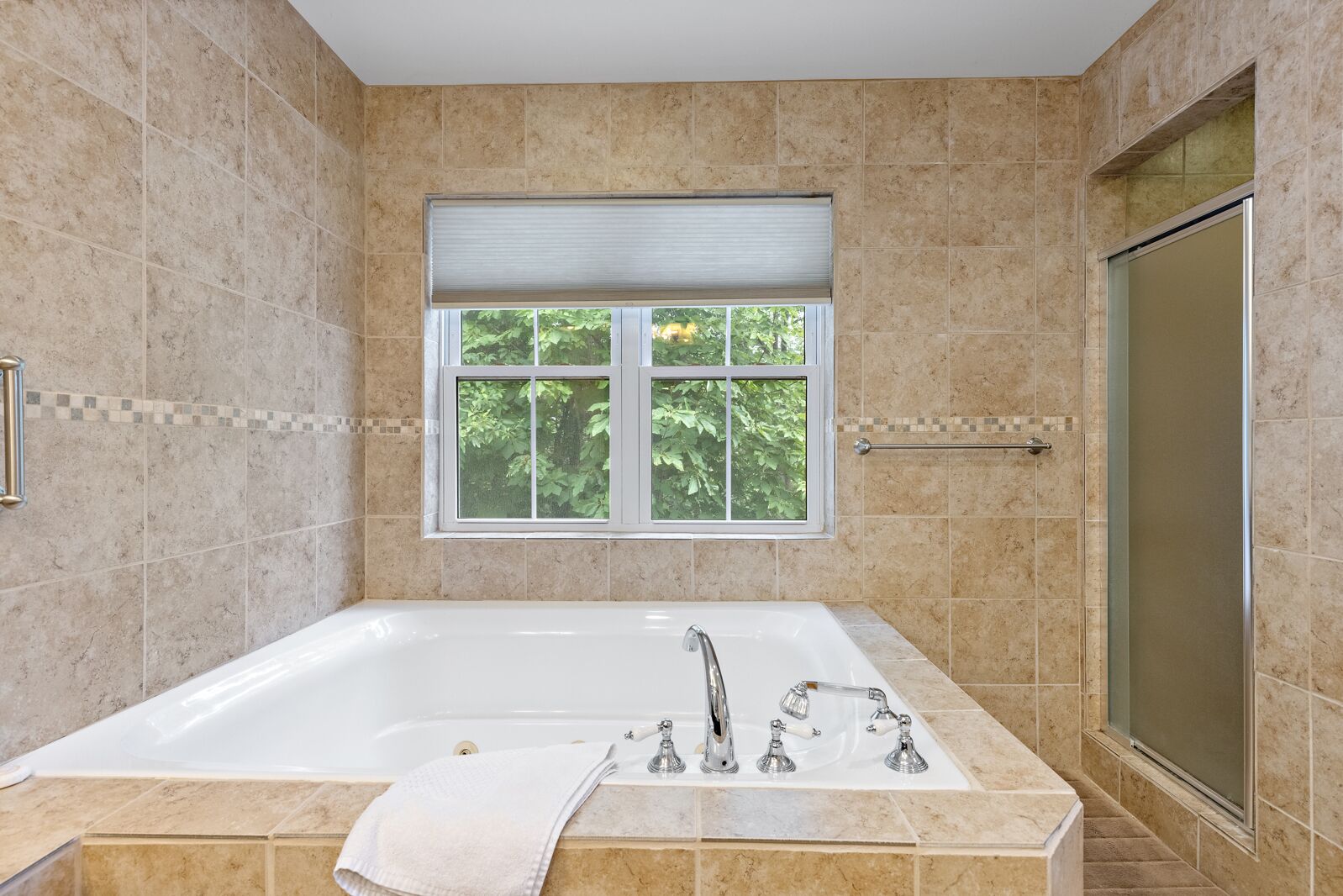 A bathroom with a large bathtub, a window with a view of trees, and a shower area.