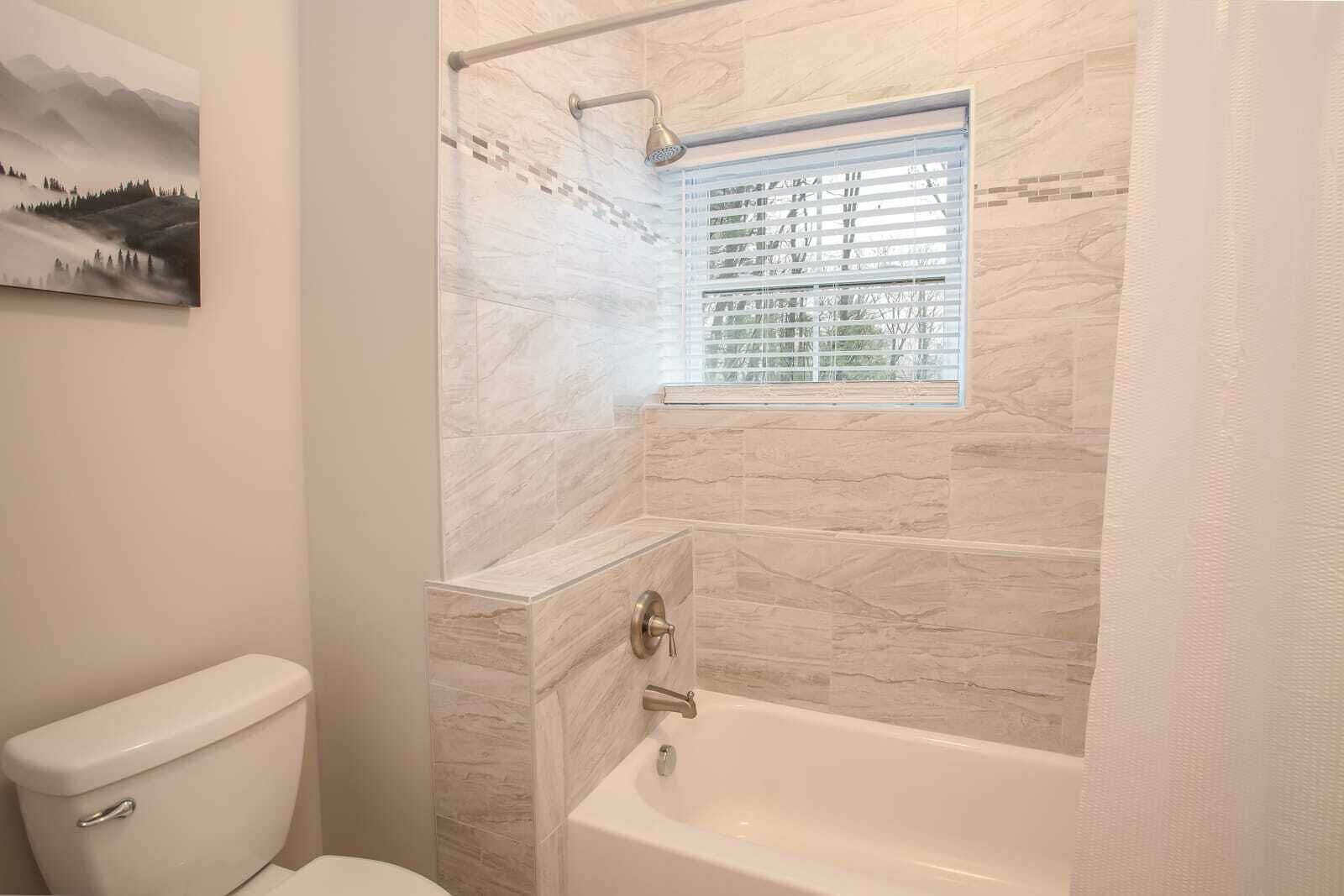 A bathroom with a bathtub, a window with blinds, and a toilet.