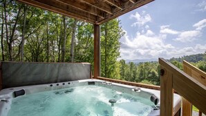 Een hottub met een houten terras en uitzicht op een bebost gebied.
