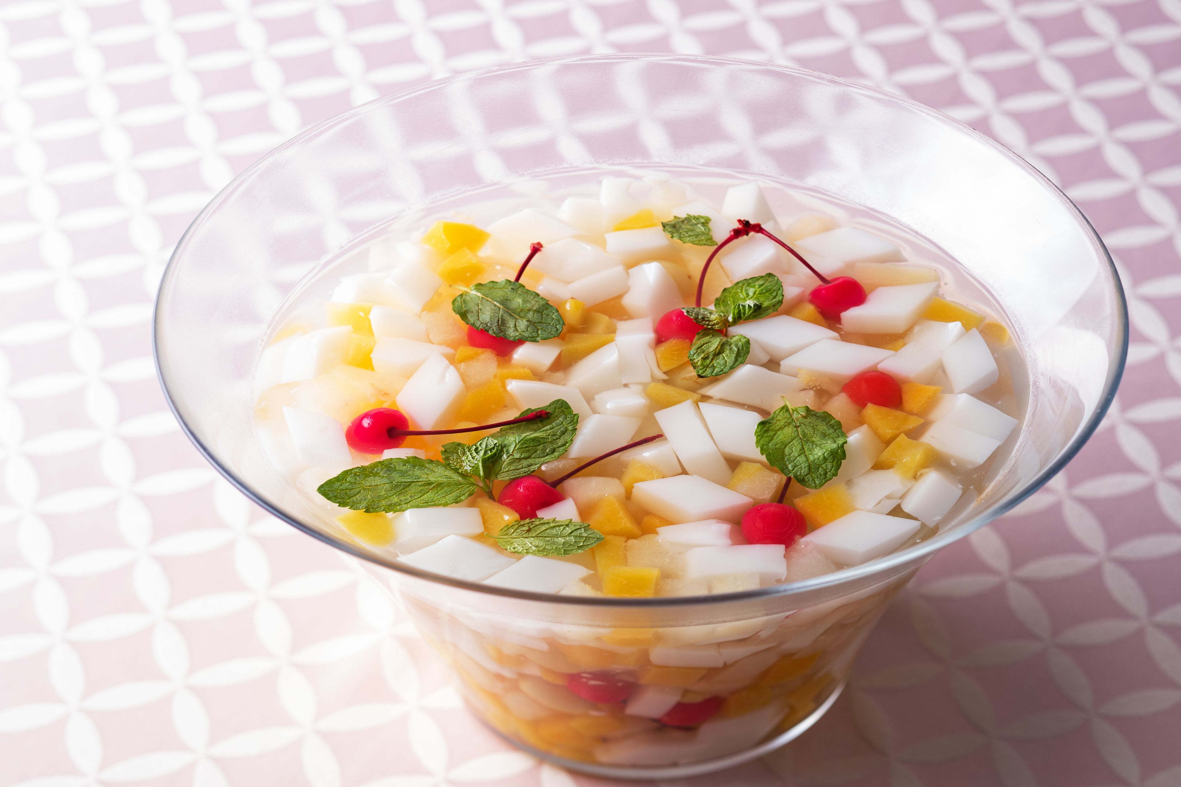 A glass of fruit salad with diced fruits and mint leaves.