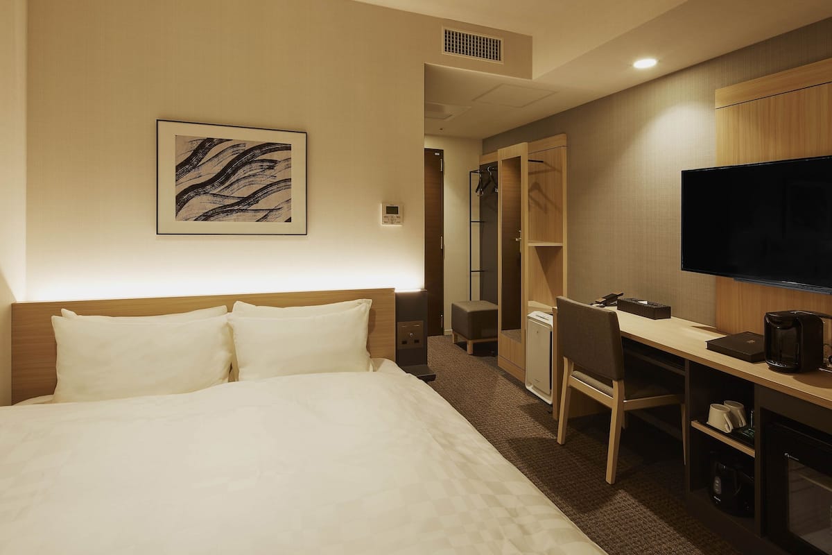 A hotel room with a bed, a desk, a chair, a television, and a coffee maker.