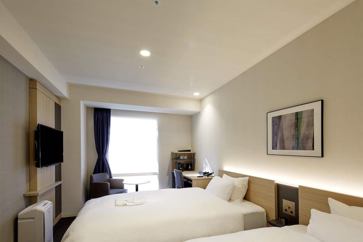 A hotel room with two beds, a TV, a desk, and a window with curtains.