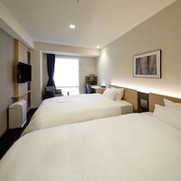 A hotel room with two beds, a TV, a desk, and a window with curtains.