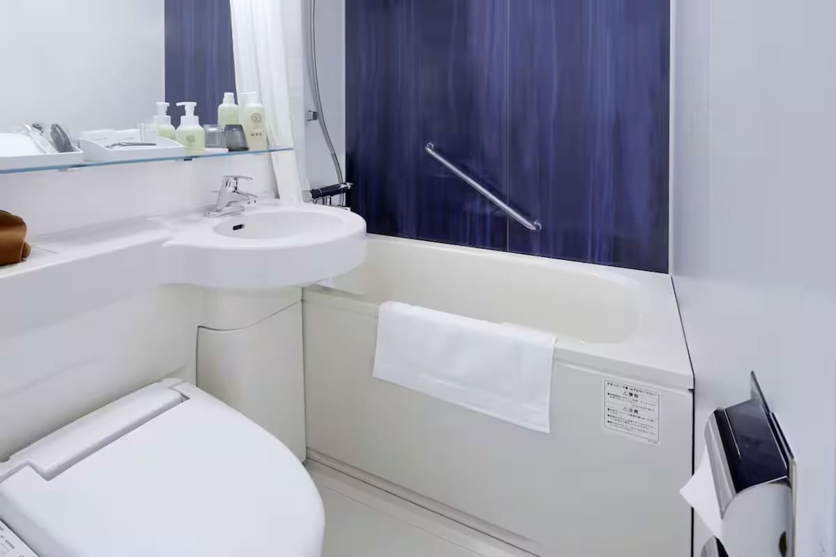 A bathroom with a white sink, mirror, and a bathtub with a white towel.