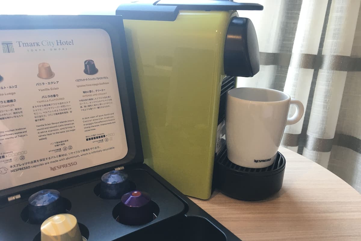 A coffee machine with a menu card, a white mug, and a green container on a table.