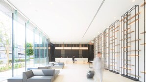 Un vestíbulo moderno con paredes de vidrio, una mesa de recepción y zonas de estar.