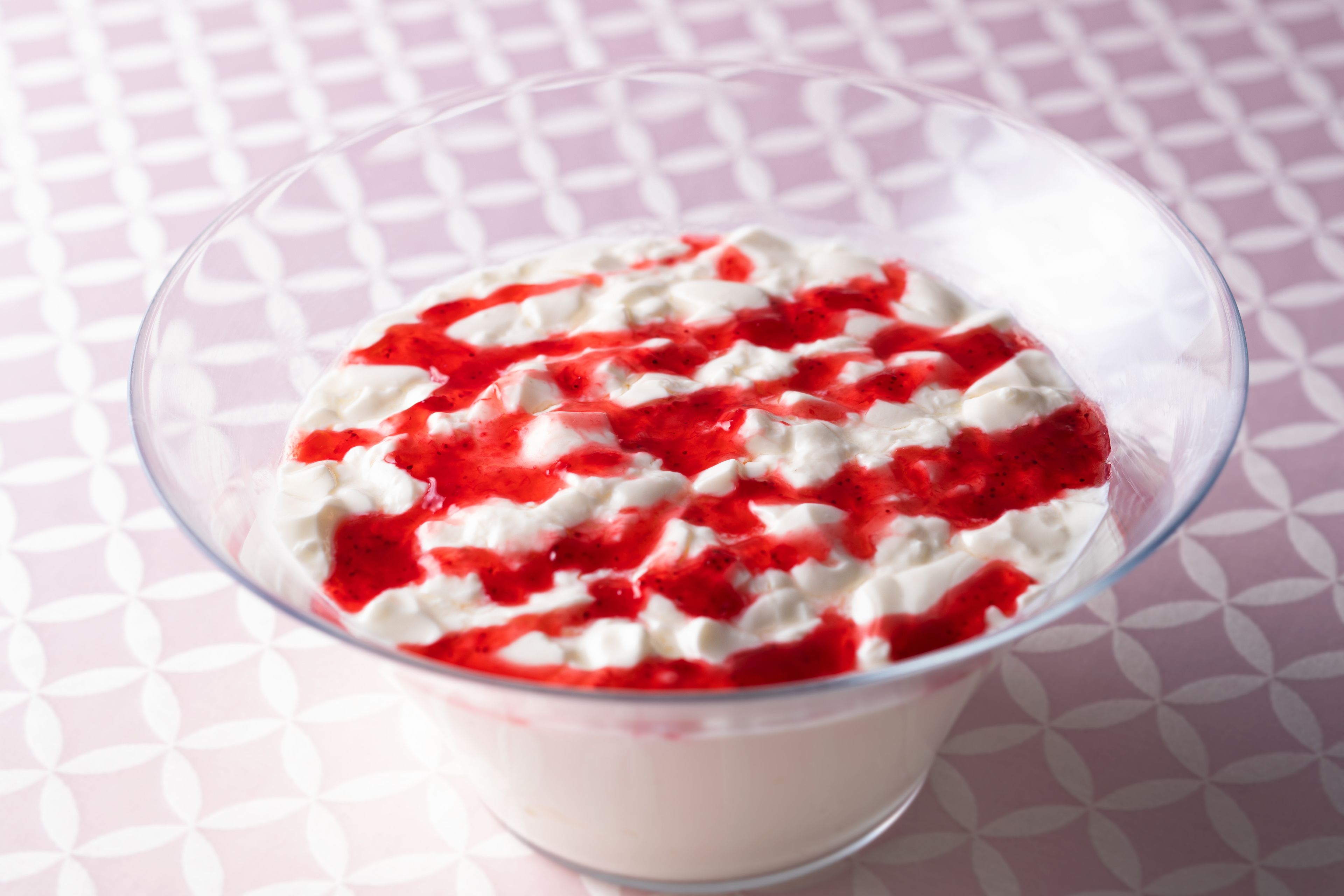 A clear glass bowl containing a white creamy dessert topped with red fruit sauce.