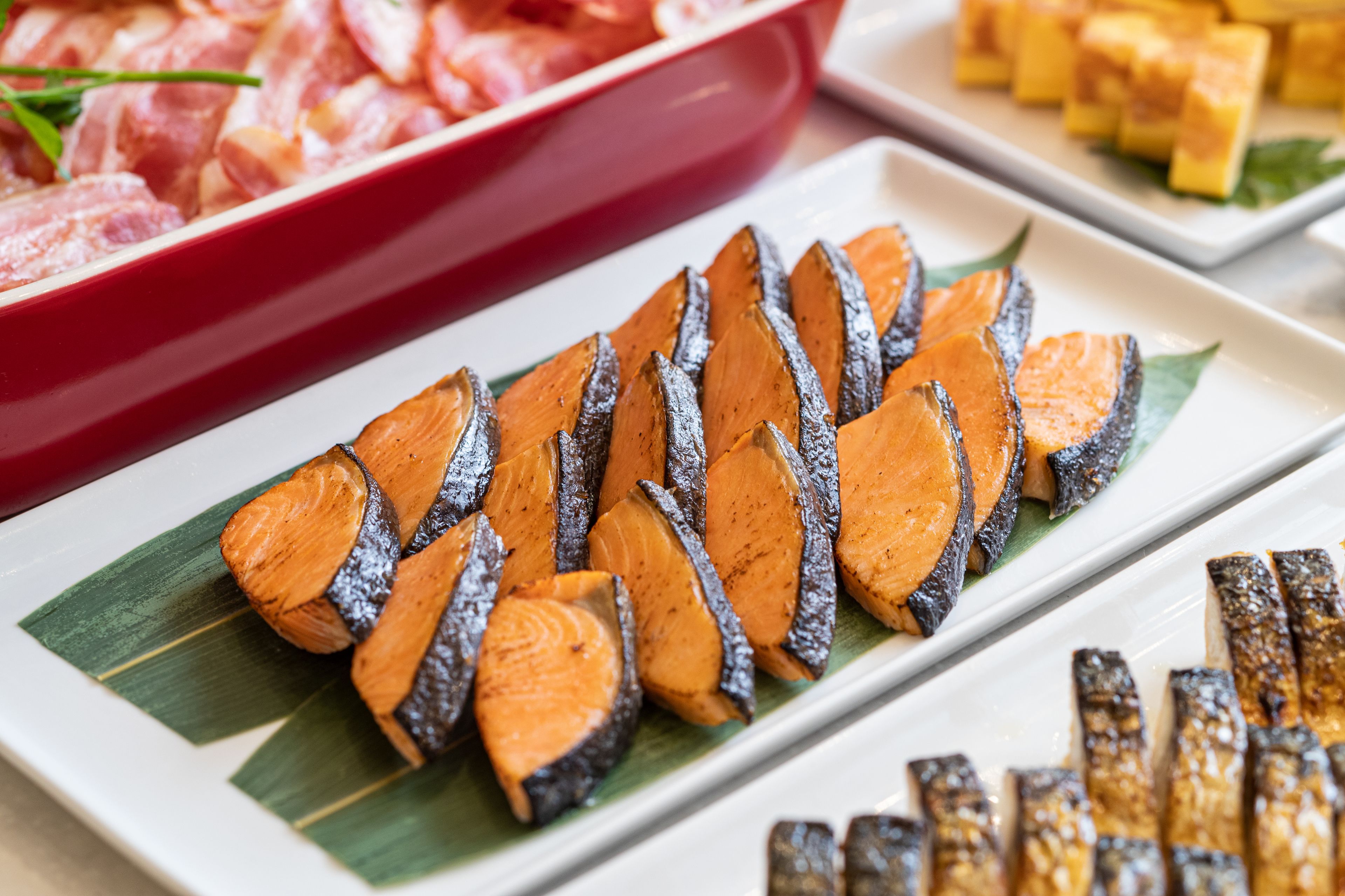 A plate of sliced sweet potatoes with a red container of meat in the background.