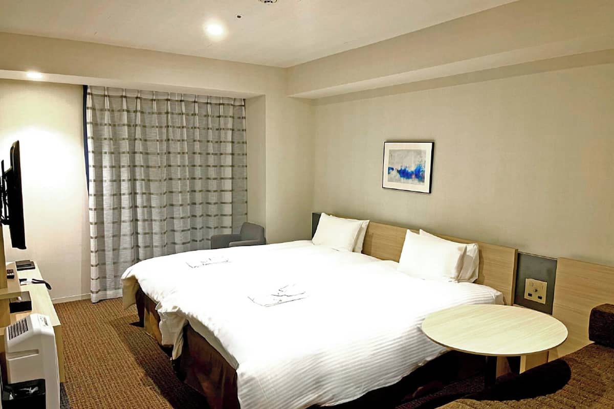 A hotel room with a large bed, a desk with a chair, a small round table, and a television.