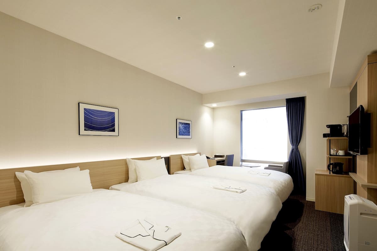 A hotel room with two beds, a desk, a chair, a television, and a window with curtains.