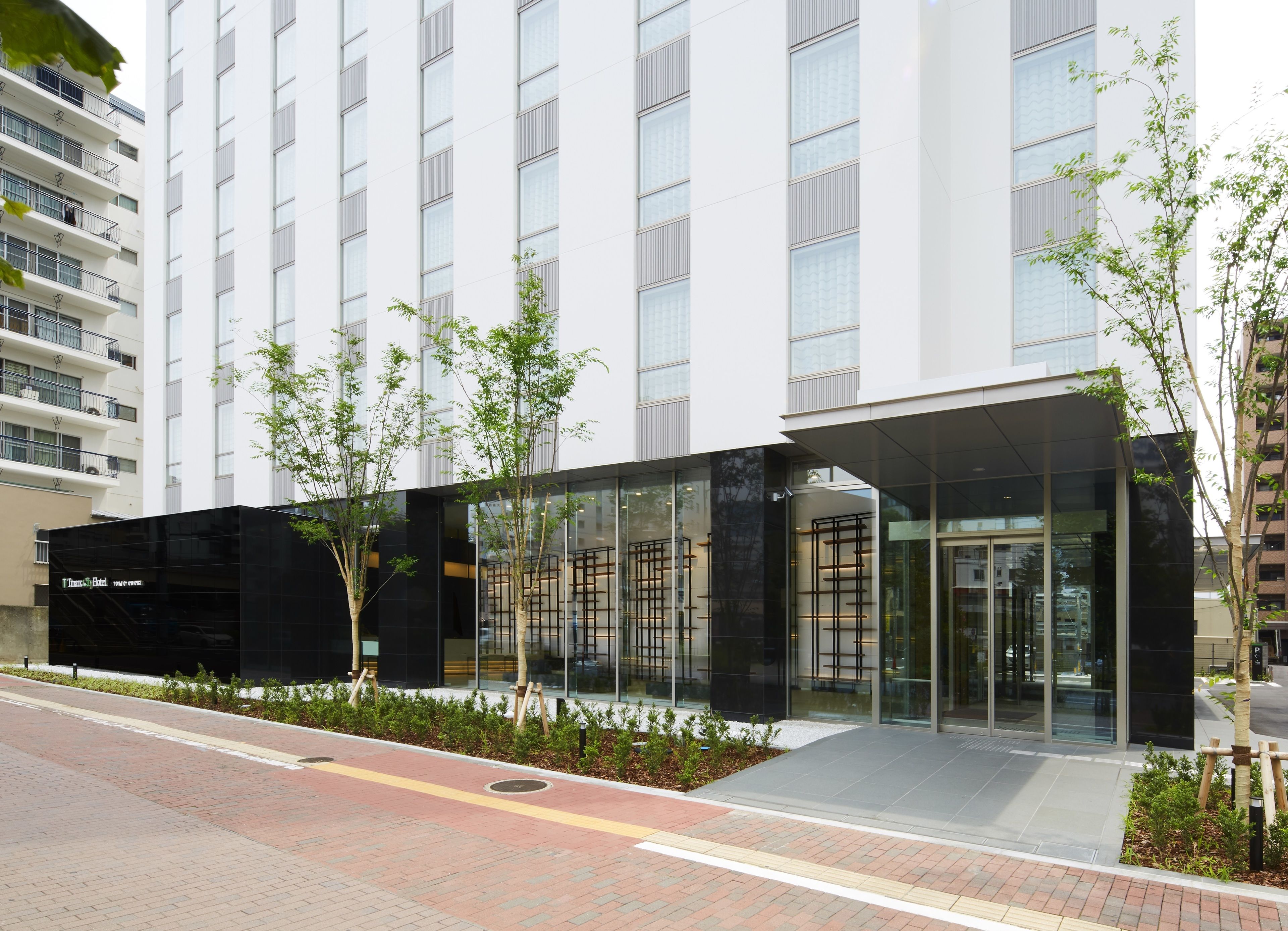 A modern hotel with a glass facade, a black entrance, and a landscaped area with trees.