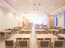 A spacious conference room with multiple tables and chairs, a reception area, and large windows providing natural light.