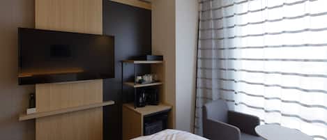 Ein modernes Hotelzimmer mit Bett, Wandfernseher, kleinem Tisch und Stuhl.