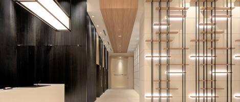 A modern hotel lobby with a reception desk, a wooden accent wall, and a series of illuminated shelves.