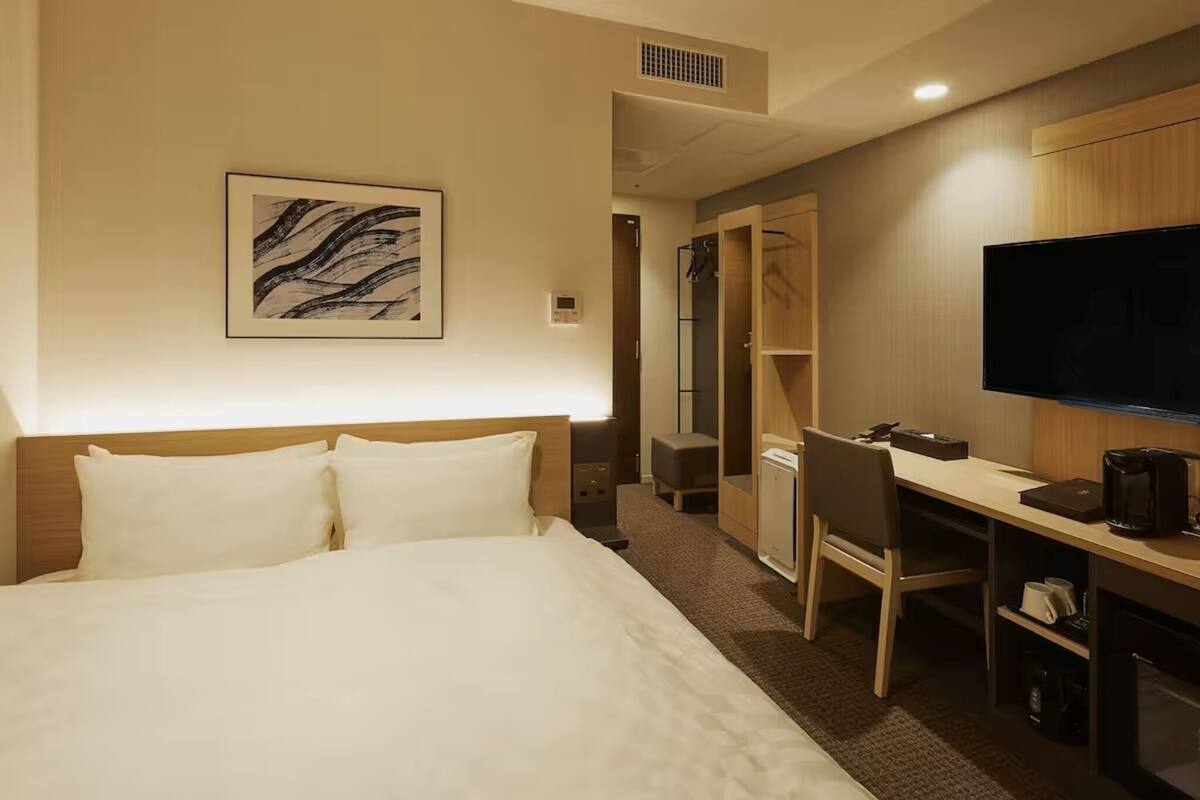 A hotel room with a bed, a desk with a chair, a television, and a wardrobe.