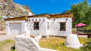 A white building with a wooden roof, a garage, and a small patio area with a red umbrella. - Adobe House on Taylor River | 3 Bedroom | River Access | Gas Grill | Yard (Almont)