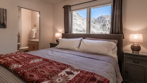 A bedroom with a bed, a window with curtains, a bedside lamp, and a view of a mountainous landscape. - Adobe House on Taylor River | 3 Bedroom | River Access | Gas Grill | Yard (Almont)
