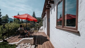 A wooden deck with outdoor seating and red umbrellas, overlooking a mountainous landscape. - Adobe House on Taylor River | 3 Bedroom | River Access | Gas Grill | Yard (Almont)