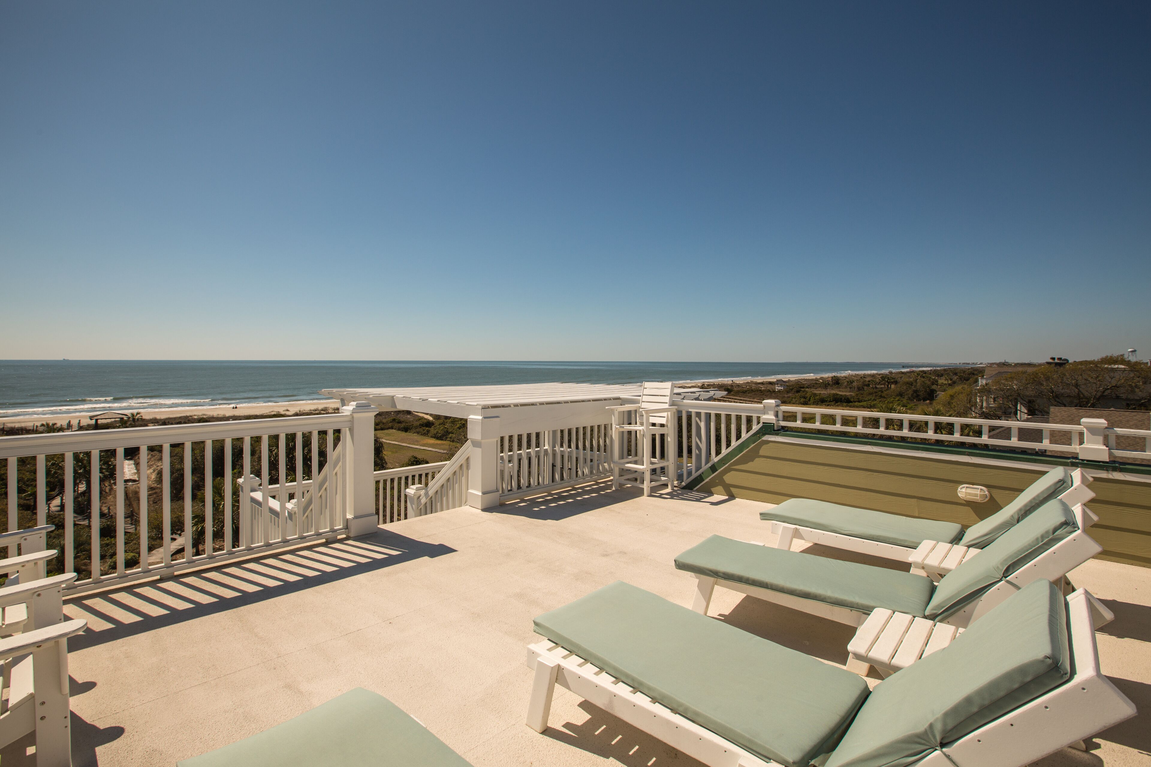 Un balcon donnant sur la plage, avec des chaises longues et une vue sur l’océan.