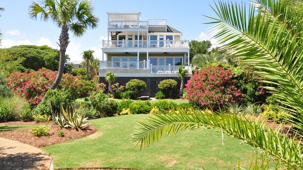 Ett tvåvåningshus med en balkong, omgivet av en välskött trädgård med olika växter och blommor.