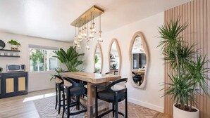 A modern dining area with a wooden table, black chairs, and hanging light fixtures.