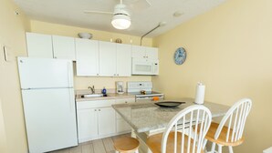 A compact kitchen with white cabinets, a microwave, a coffee maker, and a dining area with a table and chairs. - # 902 Gulf View at Lovers Key Beach Club (Bonita Springs)