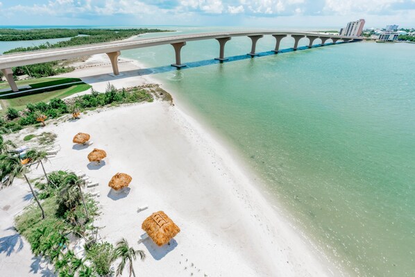 A beach with a bridge, clear water, and thatched umbrellas.