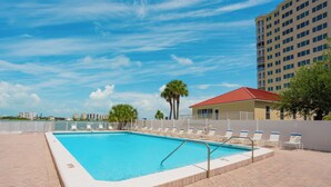 A swimming pool with lounge chairs, a red-roofed building, and a tall residential building in the background. - # 902 Gulf View at Lovers Key Beach Club (Bonita Springs)