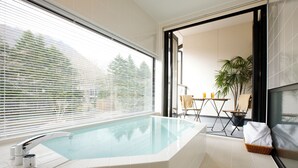 A modern bathroom with a freestanding bathtub, a window with blinds, and a view of the outdoors. - Karuizawa Hotel Longing House (Karuizawa)