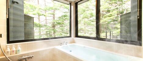 A modern bathroom with a large bathtub, a toilet, and a sink. There are three bottles of shampoo on the counter.