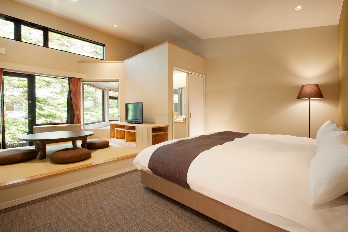 Ein modernes Hotelzimmer mit einem großen Bett, einem Fernseher, einem Schreibtisch und Blick auf Grünfläche.