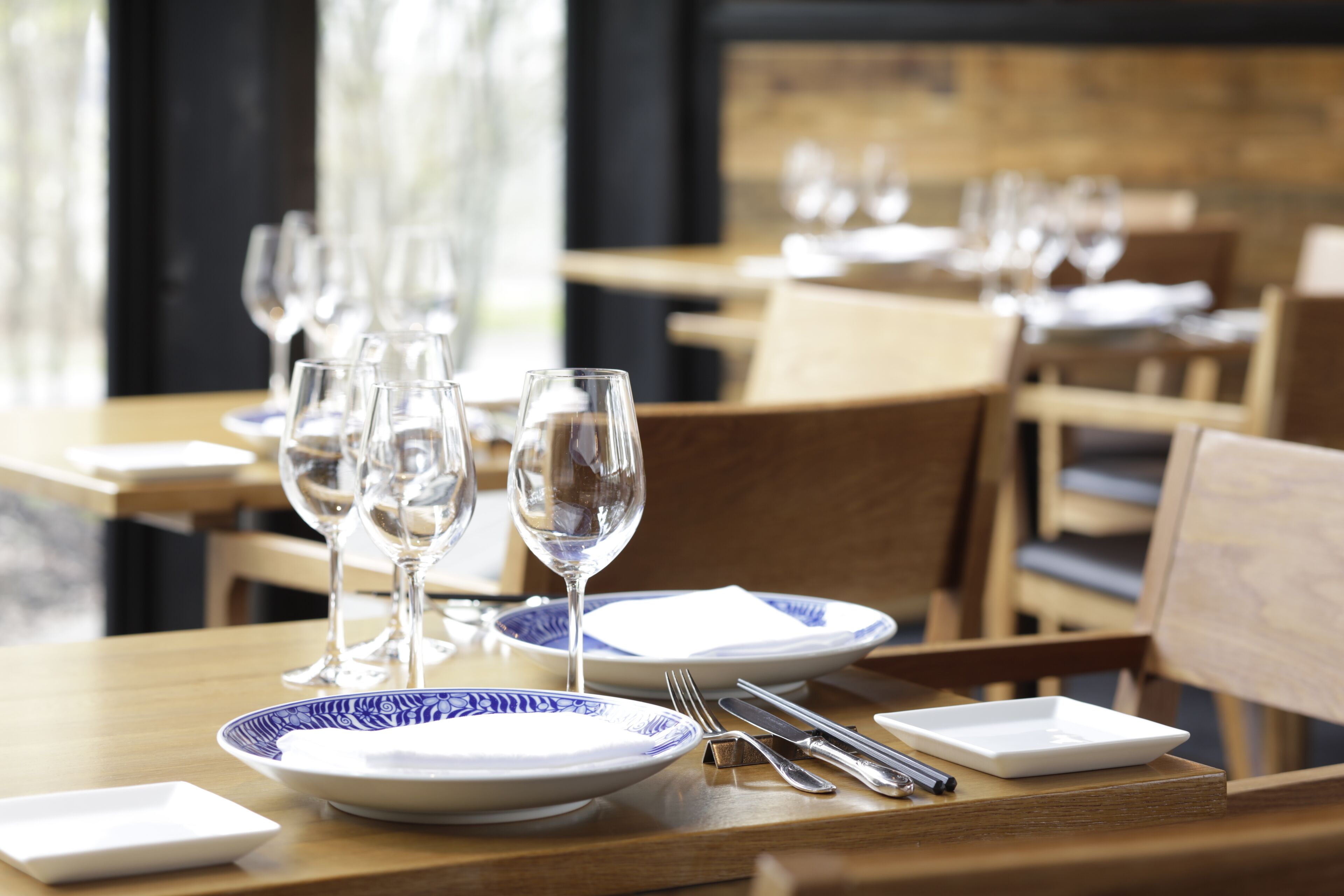 A dining table set with plates, cutlery, and wine glasses, with chairs around it.