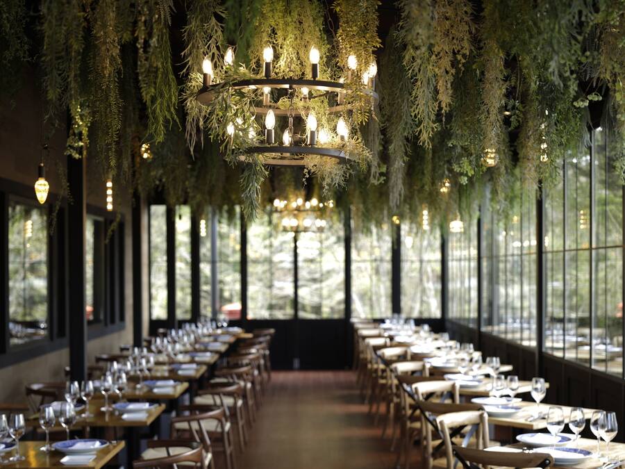 A restaurant with long tables, hanging greenery, and a chandelier.
