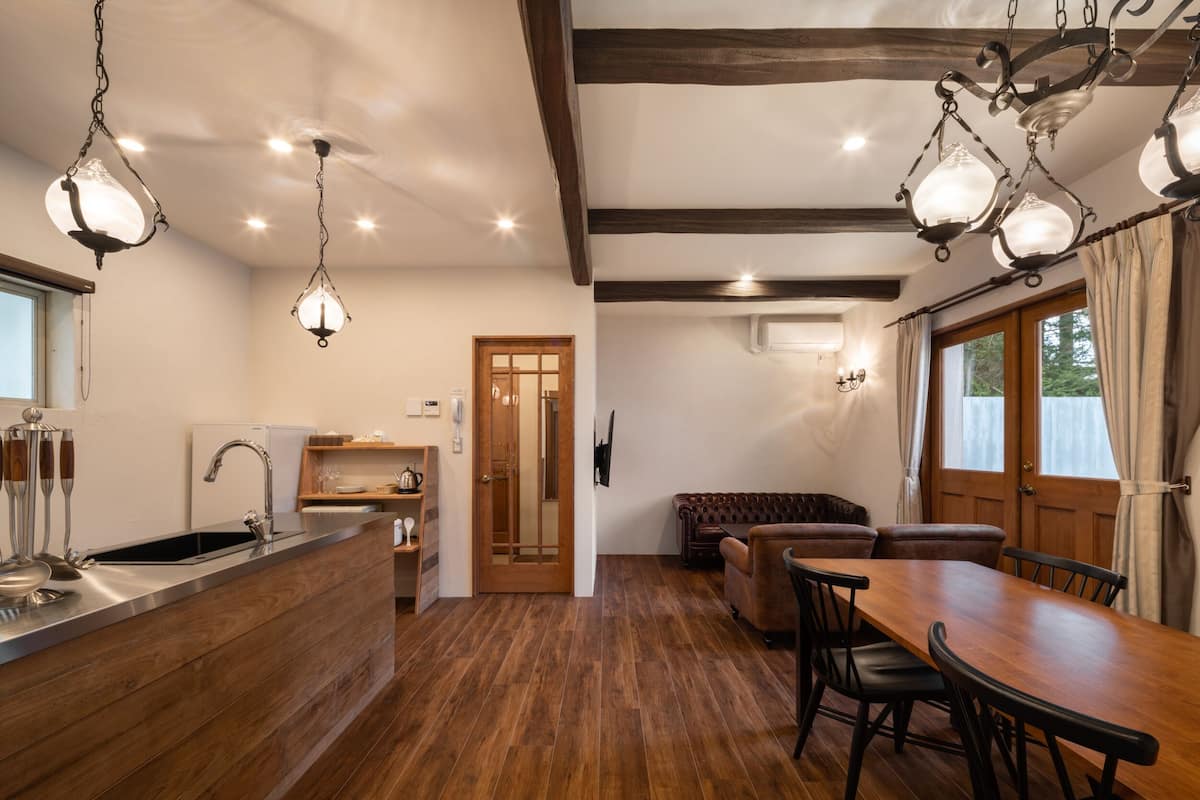 Eine moderne Küche mit Holzboden, ein Essbereich mit Holztisch und -stühlen und eine gemütliche Sitzecke mit einer braunen Ledersofa.