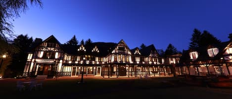 A large, illuminated building with a traditional architectural style, featuring multiple levels and a prominent entrance.