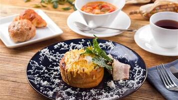 A meal with a baked item topped with cheese and greens, a bowl of soup, a croissant, and a cup of tea on a wooden table.