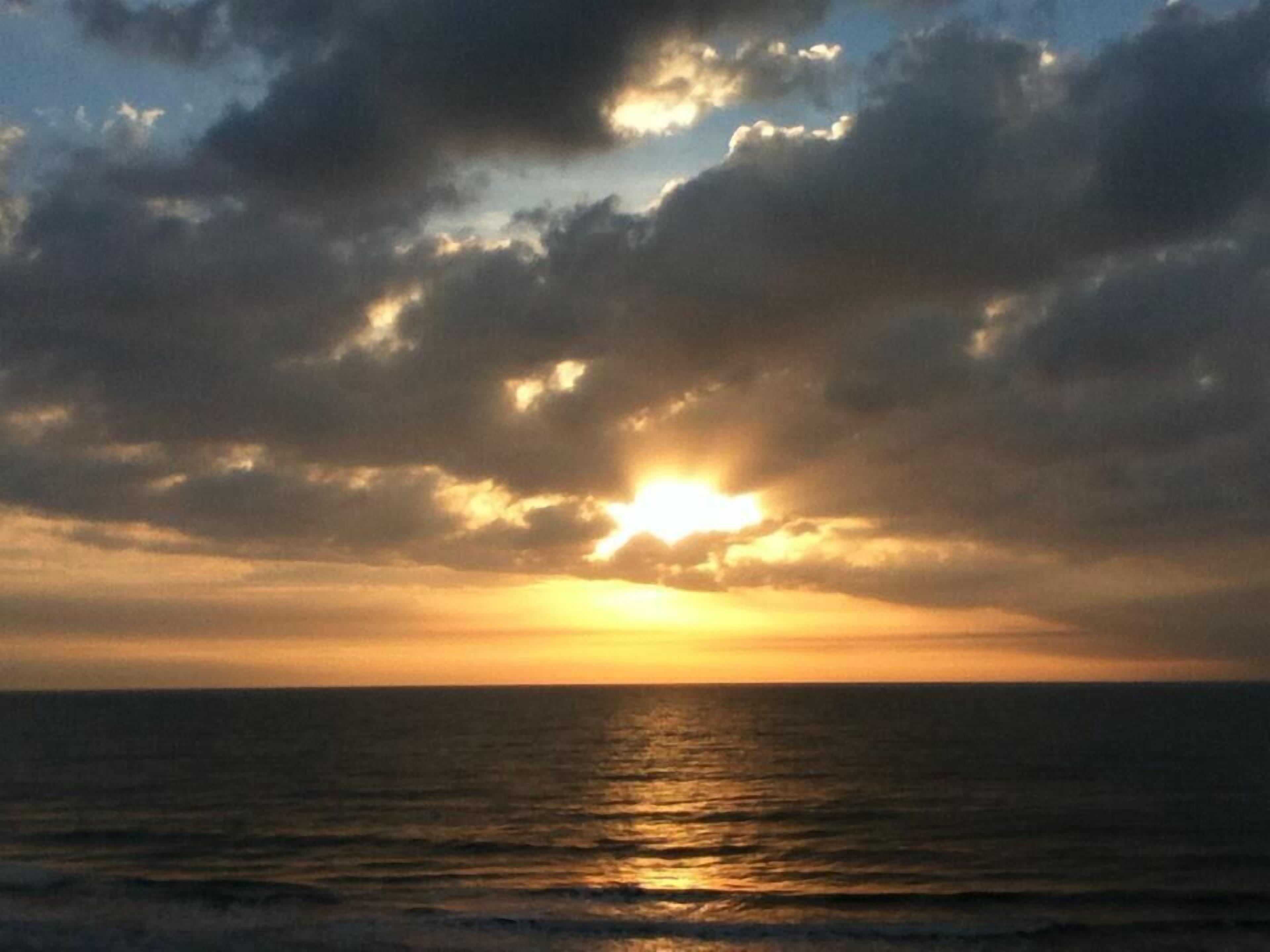 Un coucher de soleil sur l’océan, avec des nuages dans le ciel.