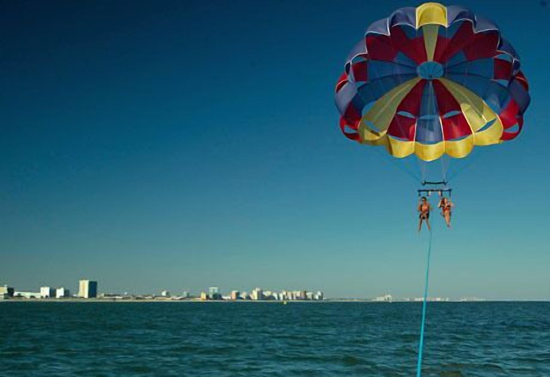 A parasail with two people over a body of water with buildings in the background.