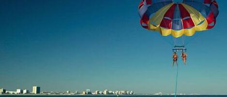 A parasail with two people over a body of water with buildings in the background.