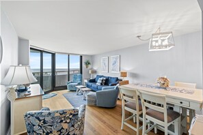 A modern living room with a sofa, chairs, a dining table, and a balcony with a view.