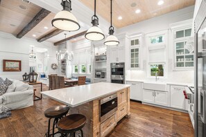 A spacious kitchen with a large island, wooden beams, white cabinetry, and a dining area with a sofa and chairs.