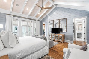 A bedroom with a large bed, a TV, and a ceiling fan.