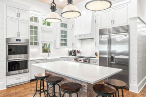 A modern kitchen with white cabinetry, stainless steel appliances, and a large island with stools. - Luxurious WaterColor Estate! Private Pool, Carriage House, Near Beach! Ideal For Large Groups! (Santa Rosa Beach)