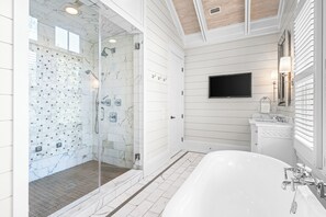 A modern bathroom with a glass-enclosed shower, a large bathtub, and a mounted TV.